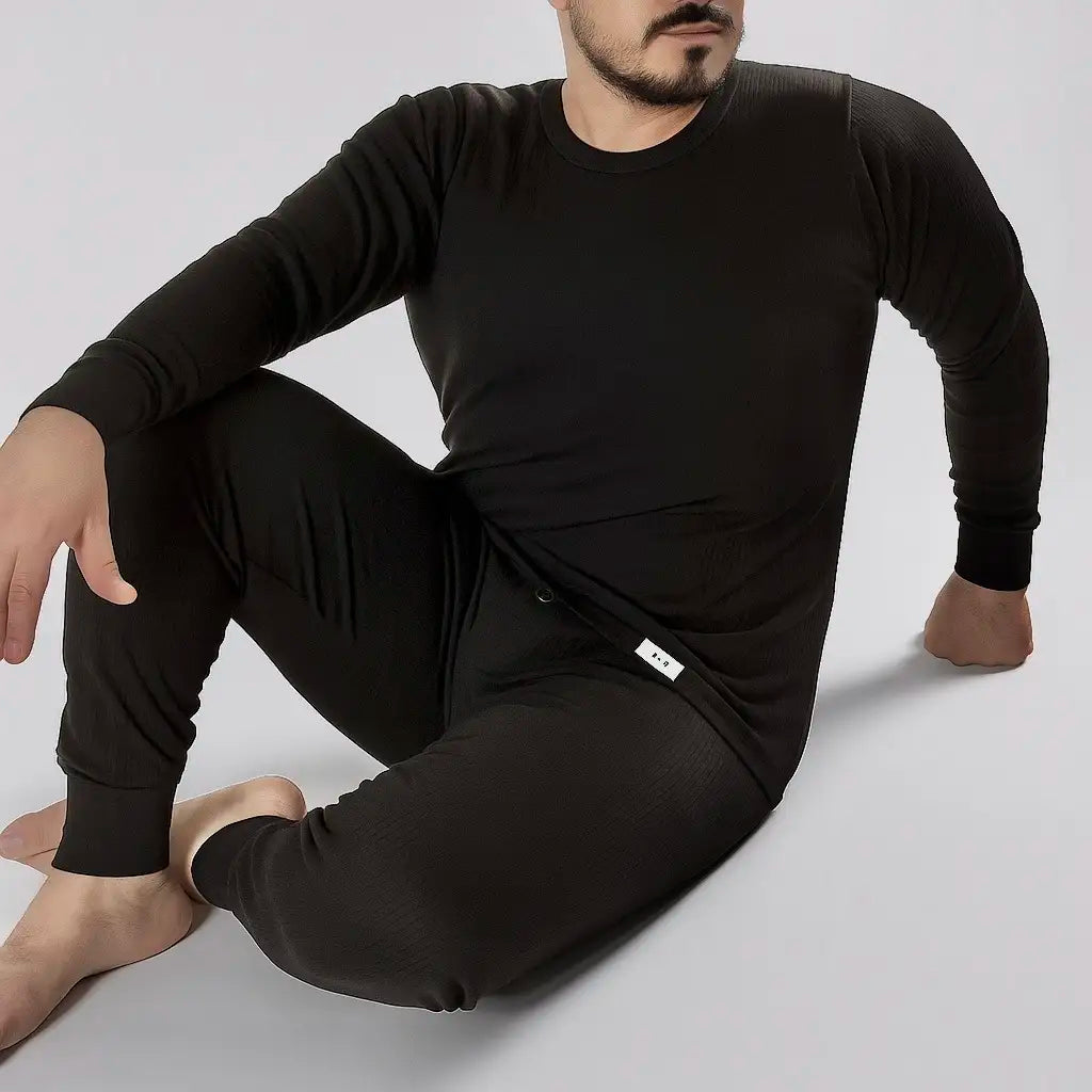 Mann sitzt entspannt im schwarzen Herren Thermounterwäsche Set aus Baumwolle, gezeigt als bequeme Loungewear.